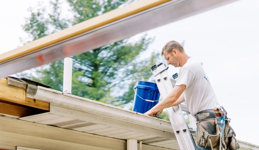 Gutters-1 Valley Roofing team member on a ladder and cleaning out gutters.