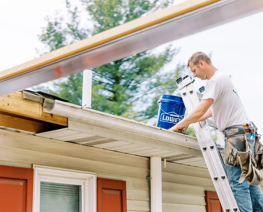man cleaning gutters on ladder