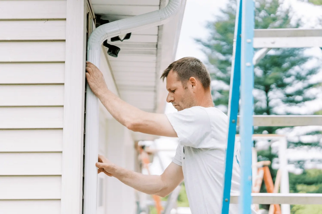 Gutters-1-1 Valley Roofing team member attaching new gutters to a house.